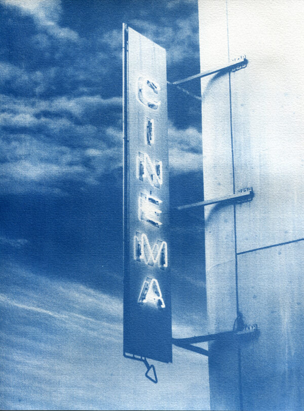 Gros plan d'un néon d'un cinéma avec écrit "cinéma" et le ciel nuageux en arrière-plan.