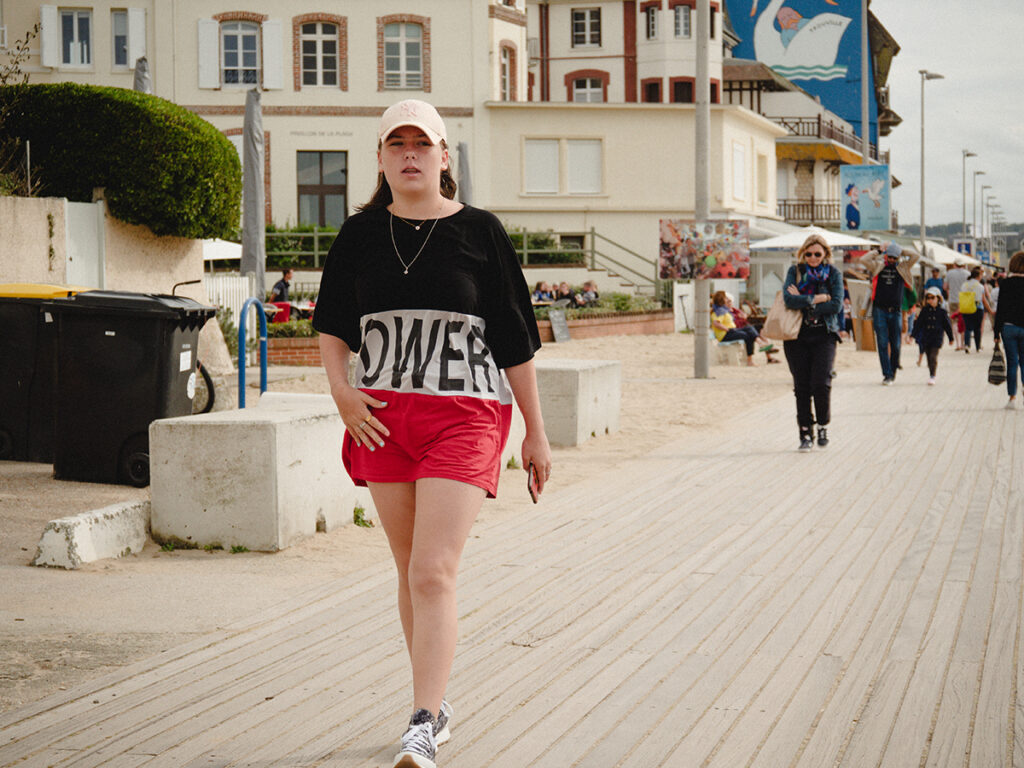 Adolescente déterminée qui marche sur la promenade de Trouville. Elle porte un t-shirt avec écrit "power" et une casquette.