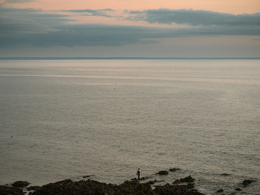Homme en train de pêcher en contrebas de la falaise. Grand angle vers l'océan avec la nuit qui tombe.