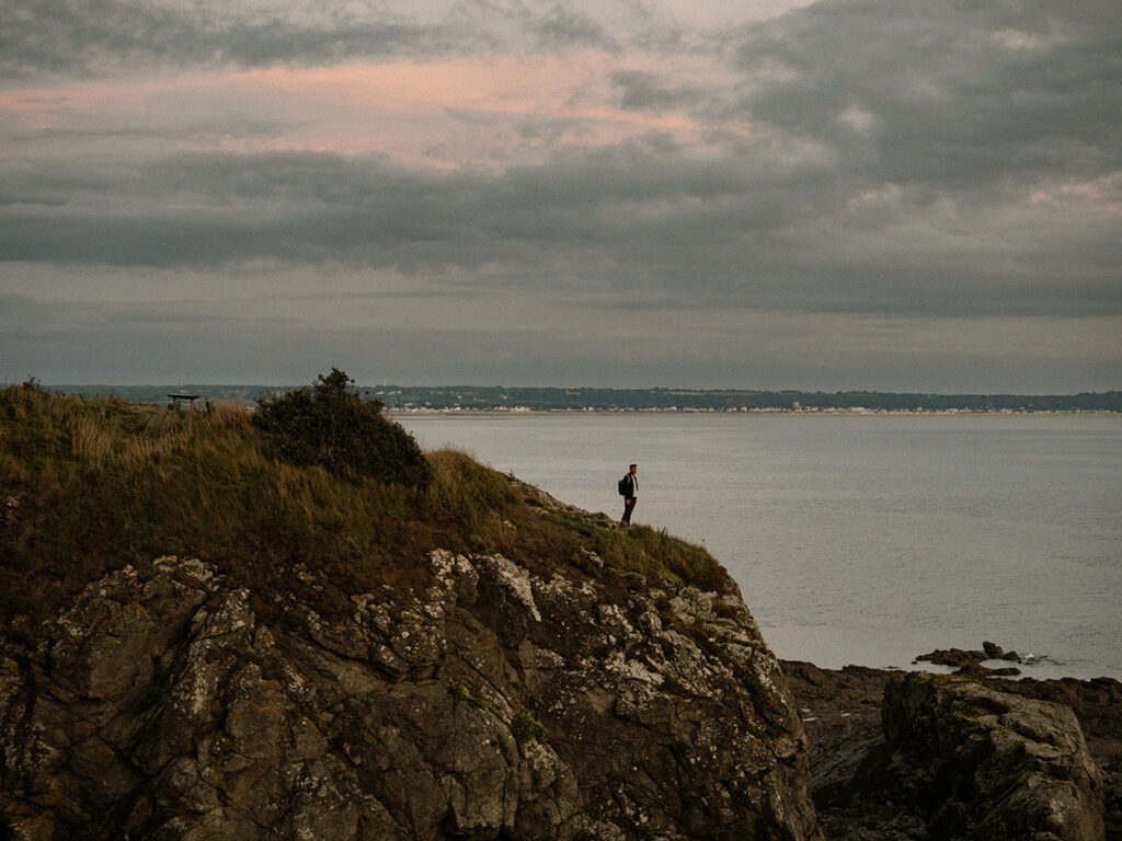 Homme debout sur la falaise qui contemple l'océan à la nuit tombée.