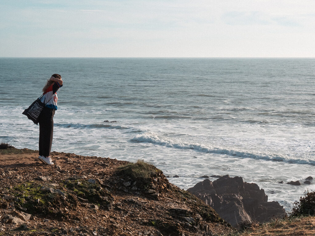 Jeune fille sur la pointe des pieds et face à l'océan en train de regarder au-delà de la falaise.
