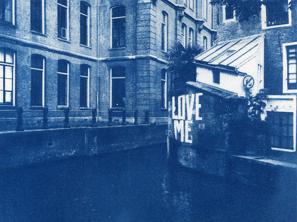 Canal circulant entre des immeubles en briques. Un graffiti "love me" est dessiné sur l'un des murs.