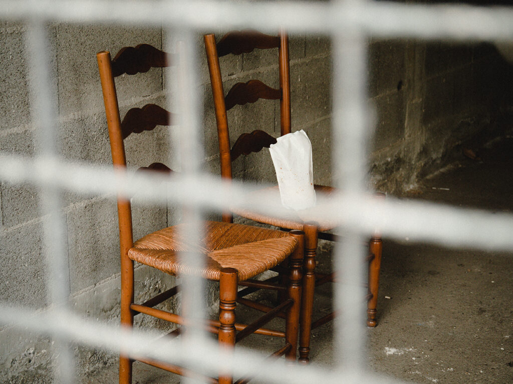 Paire de chaises en bois et assise en paille dans un garage vide derrière une grille.