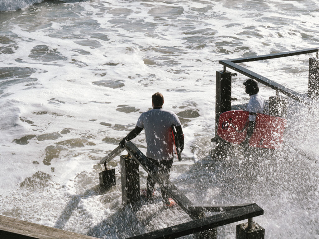 Deux jeunes hommes s'apprêtent à se lancer dans l'océan avec leurs planches alors même que la grande marée d'équinoxe a envahi la plage.