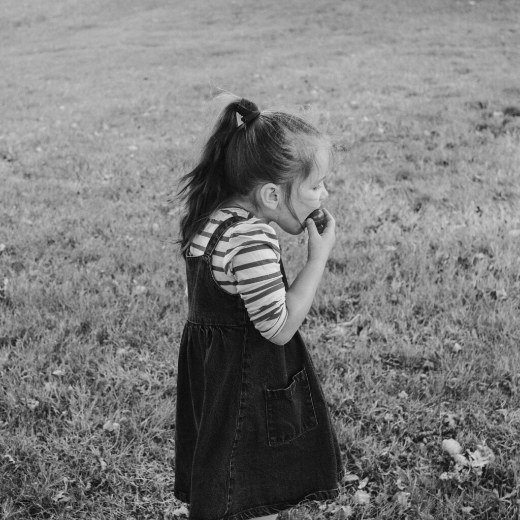 Portrait d'une petite fille à hauteur d'adulte qui est en train de manger une tomate cerise, un peu comme si elle était prise en flagrant délit.