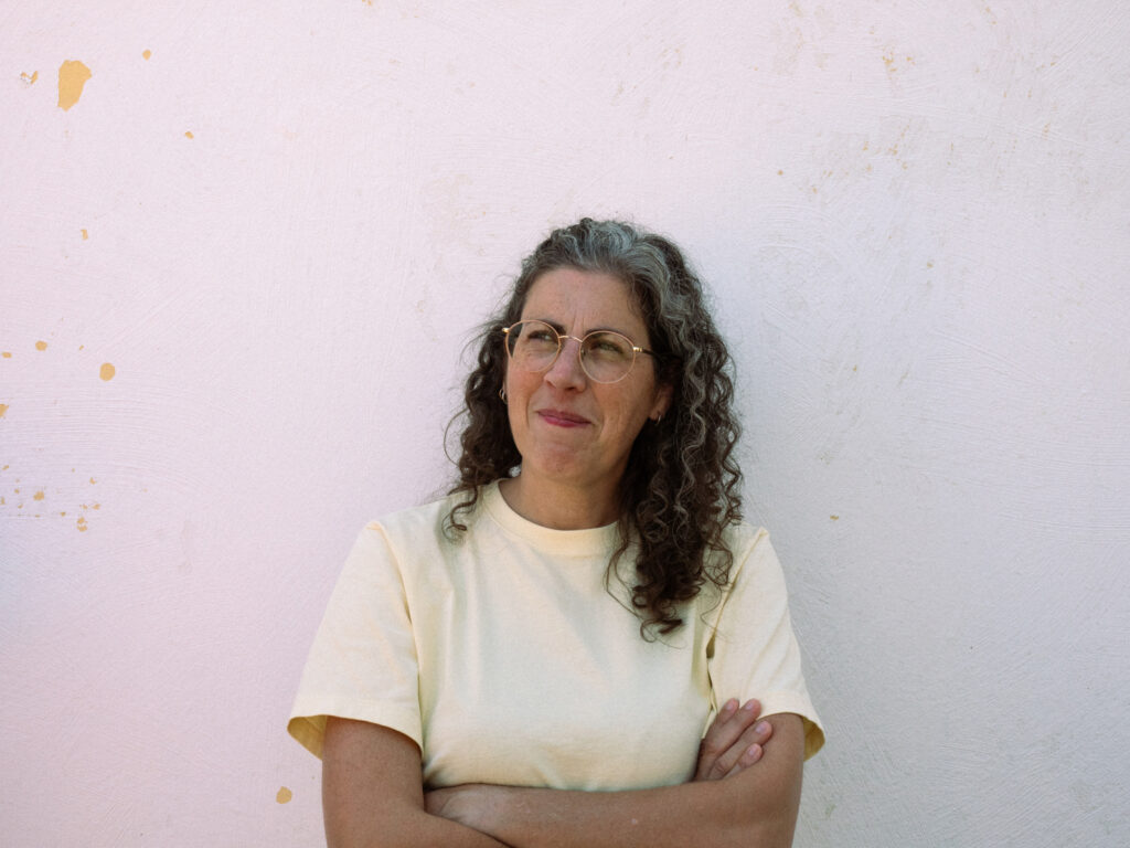Portrait d'une femme à lunettes et aux cheveux bouclés qui a les bras croisés et le regard mutin.
