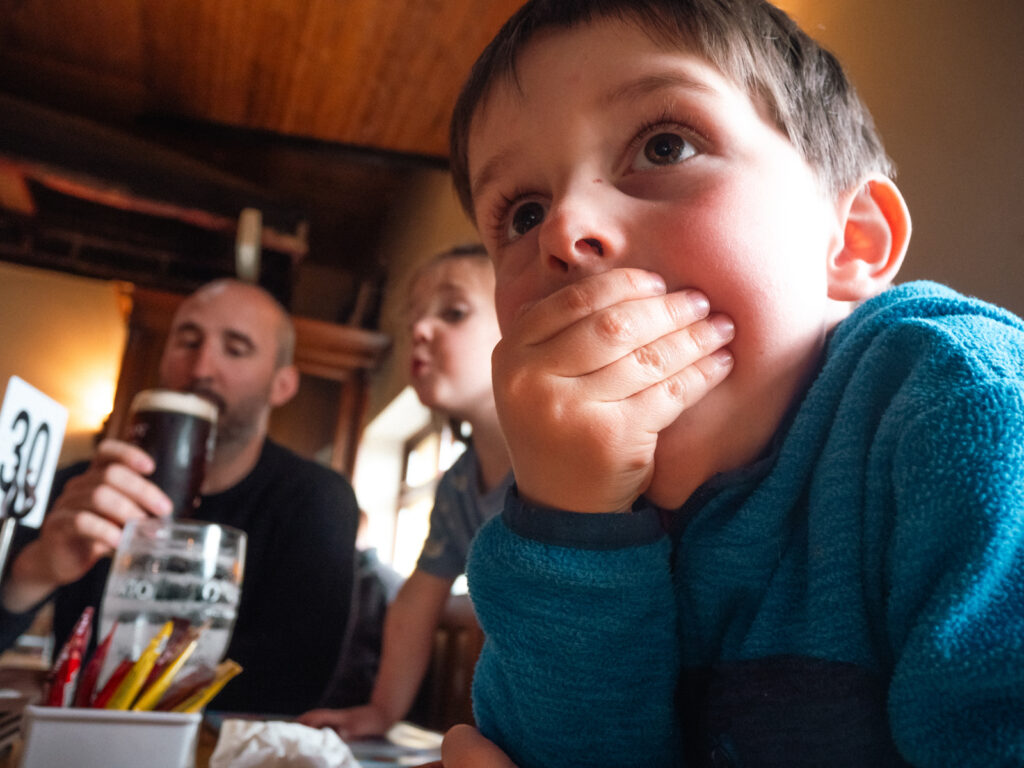 Un petit garçon porte la main à sa bouche, il est vraiment très surpris. Sa petite soeur est derrière lui, la bouche en coeur, et leur père s'apprête à boire sa Guinness en arrière-plan.