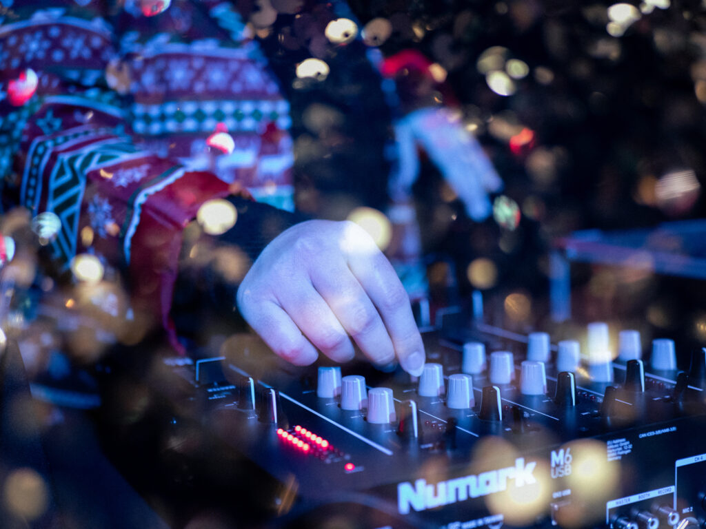 Les mains d'une DJ sur sa mixette avec une double exposition laissant apparaître des paillettes.