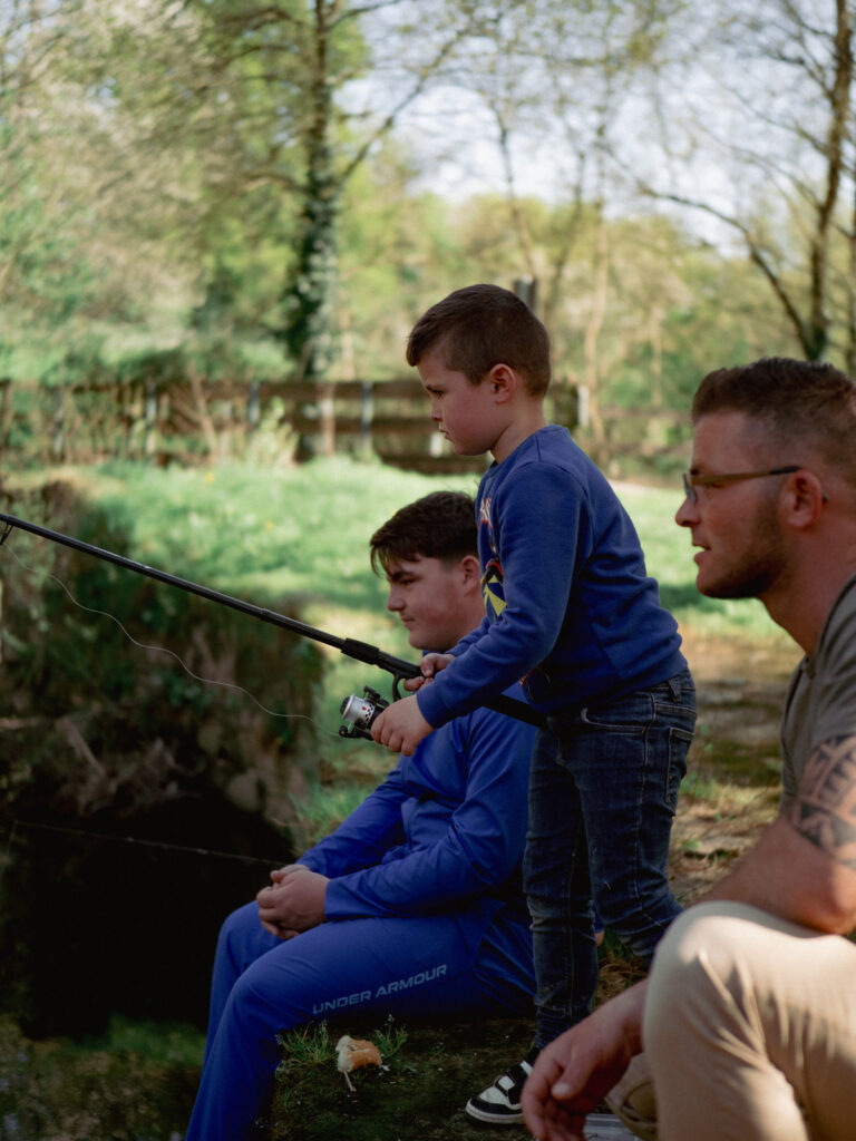 Trois personnes en train de pêcher dans un parc : un homme et son petit garçon, c'est lui qui tient la canne à pêche, et un troisième larron, un jeune homme.