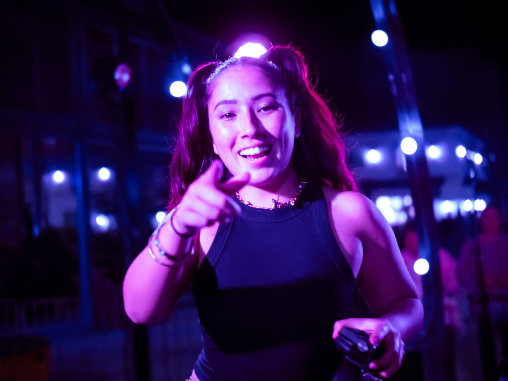 Portrait de DJ Mune sous une lumière rosée, elle pointe l'objectif du doigt.
