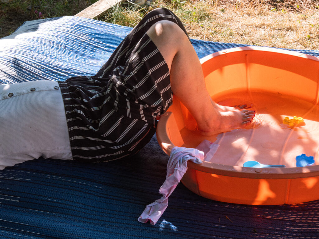 Une jeune femme dont on ne voit que les jambes les trempe dans une piscine pour bébé.