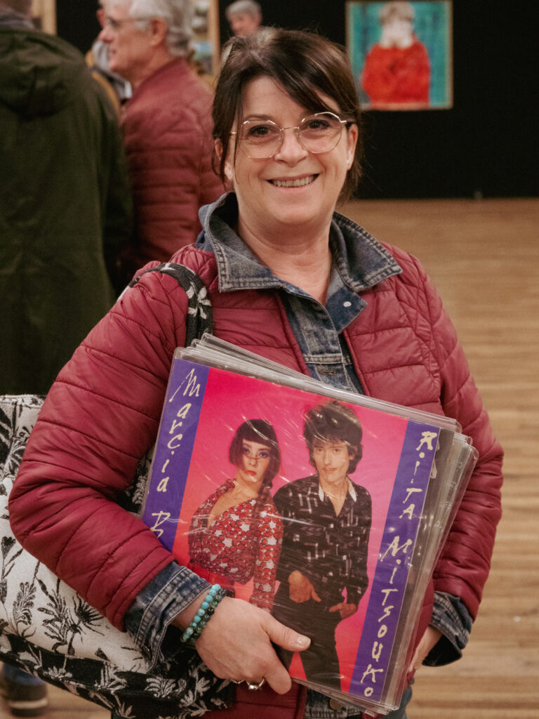 Portrait d'une femme d'un âge certain tout sourire tenant le vinyle Marcia Baila de Rita Mitsouko.