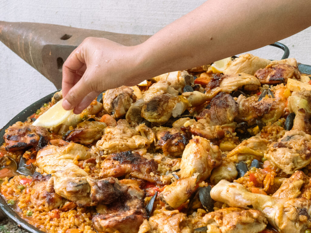 Une main munie d'un quartier de citron se penche sur une paella.