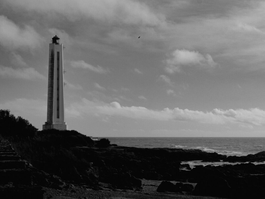 Photo en noir et blanc d'un haut phare blanc en bord de côte.