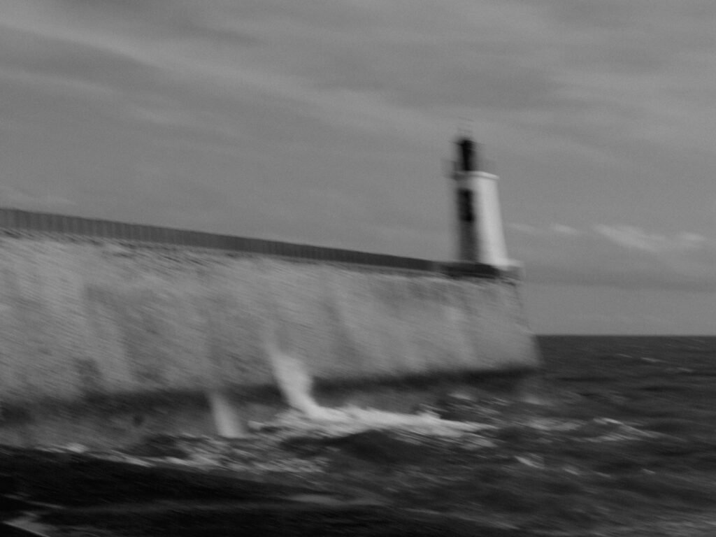 Photo en noir et blanc du phare au bout de la jetée, avec un flou de bougé intentionnel.
