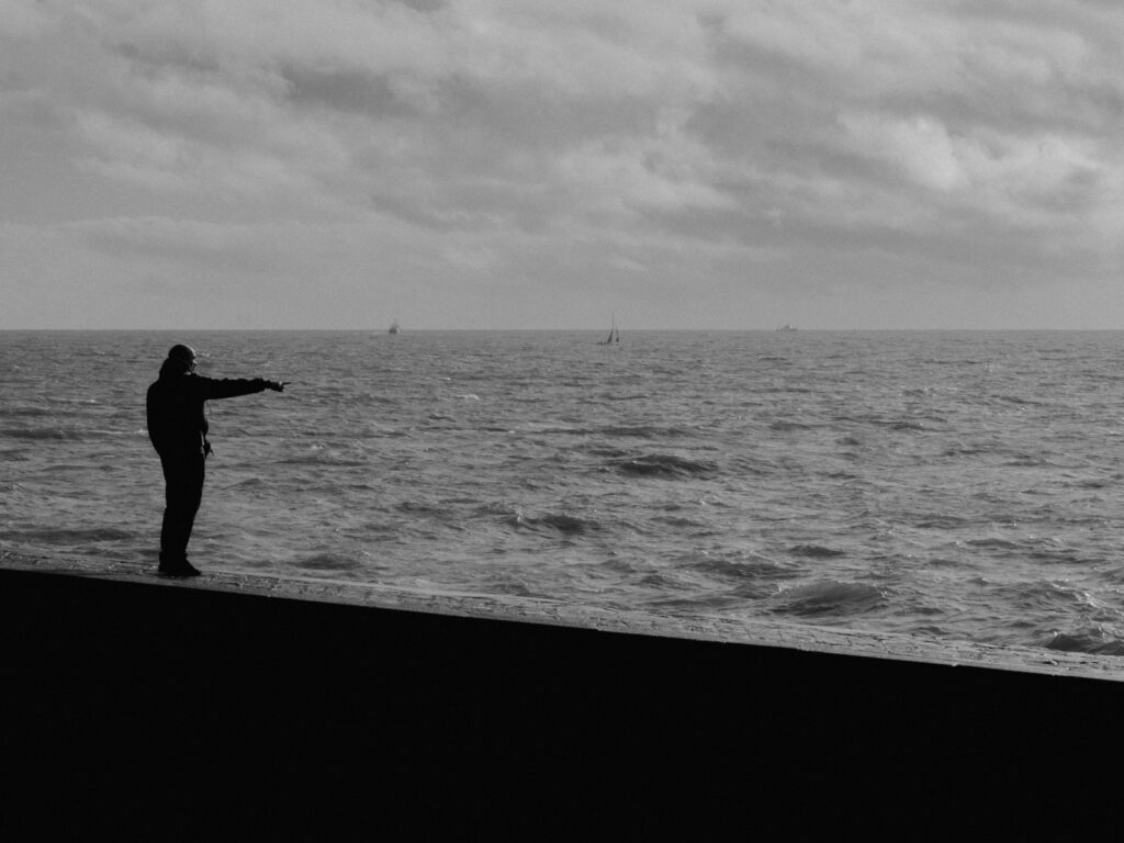 Photo en noir et blanc d'un homme, sur la jetée, qui pointe quelque chose du doigt.